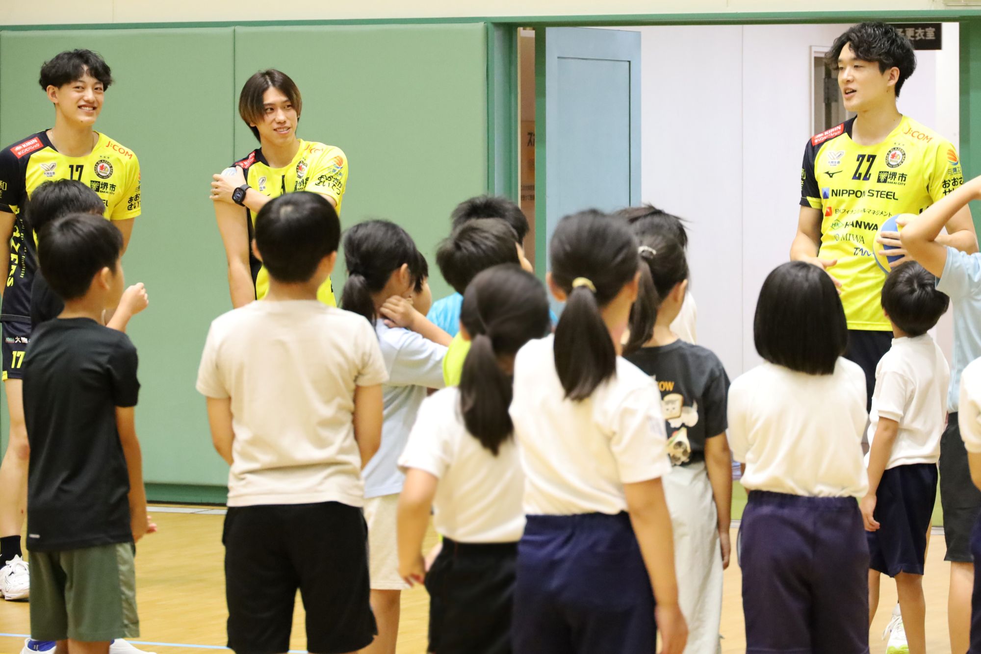子どもたちにアンダーハンドパスとレシーブの説明をするブレイザーズの選手　向かって右から、柿崎選手、大宅選手、上村選手