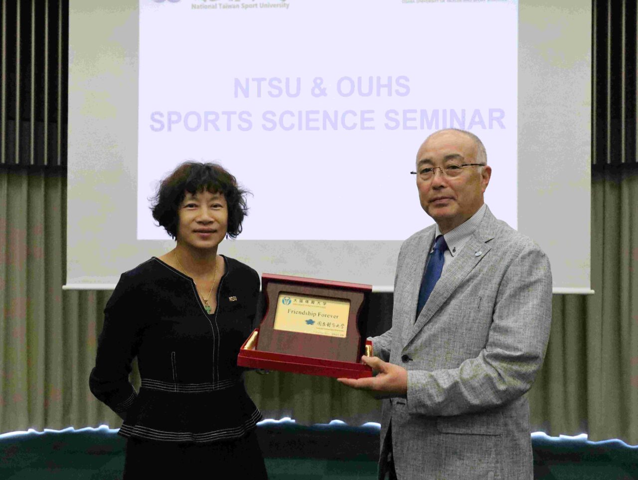 「Friendship Forever」と記された記念品を交換する神﨑浩学長と湯文慈競技学部長 【大阪体育大学】