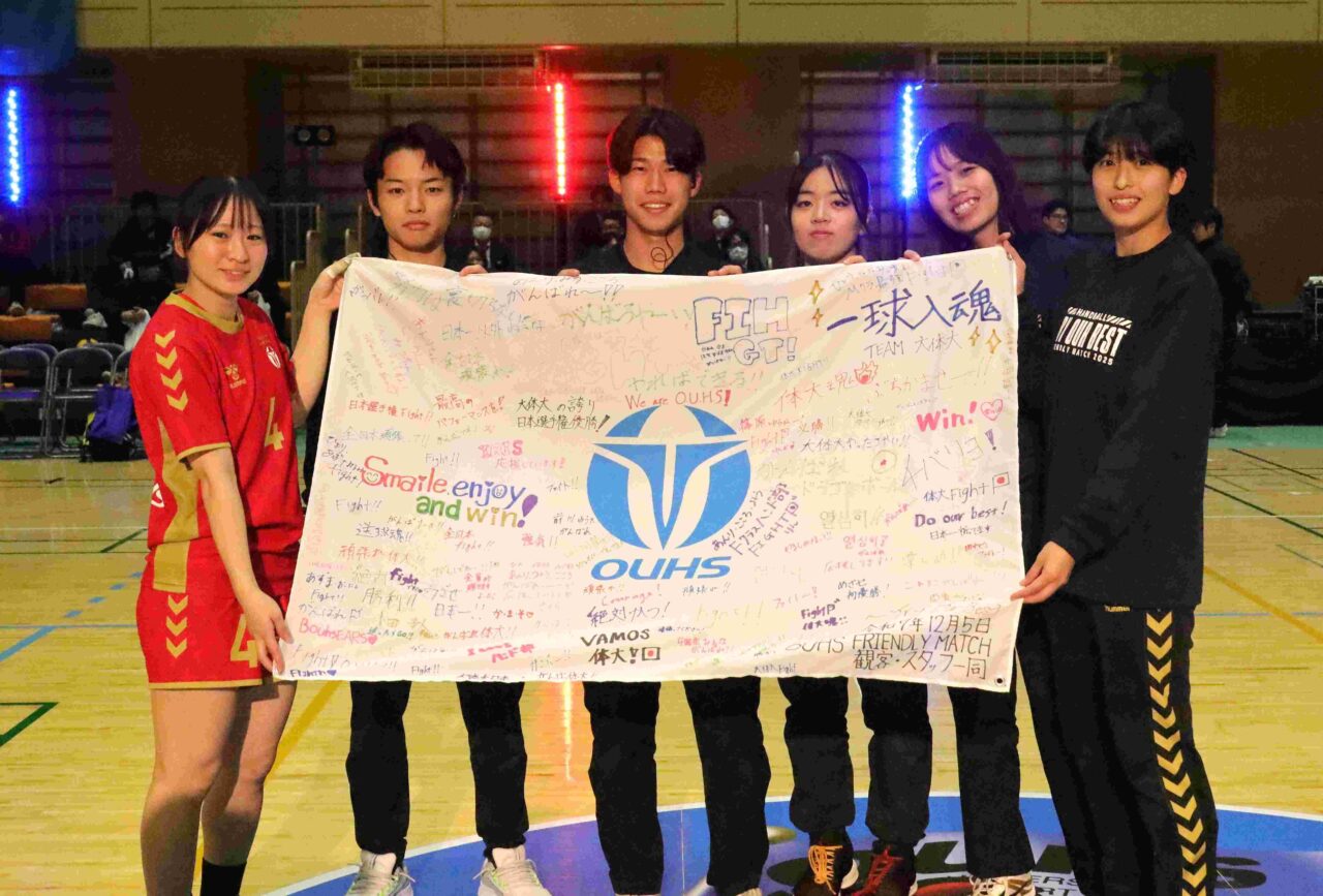 観客が応援メッセージを寄せ書きした横断幕を披露する選手と学生スタッフ 【大阪体育大学】