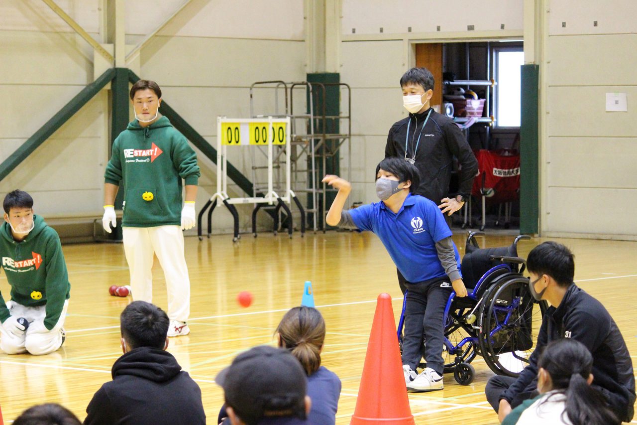 ボッチャのデモンストレーションをする内田峻介さんとその後ろで見守る曽根裕二准教授