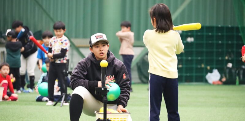 地域の方と楽しむイベントOUHSスポーツキャンプ(2025年3月)で子どもにバッティングを教える硬式野球部女子部員。各クラブが独自に社会貢献活動に取り組んでいる 【大阪体育大学】