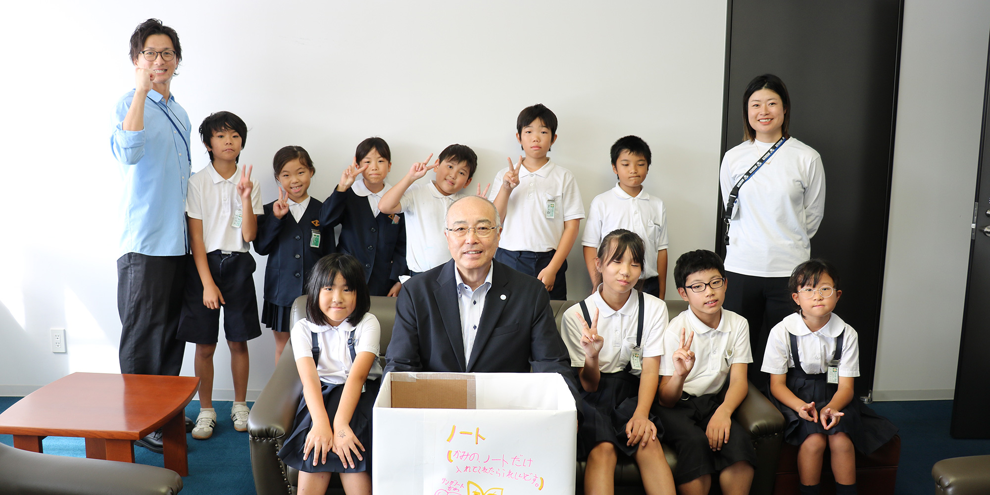 神﨑浩学長と児童たち、本学OBの辻内正輝教諭（左）