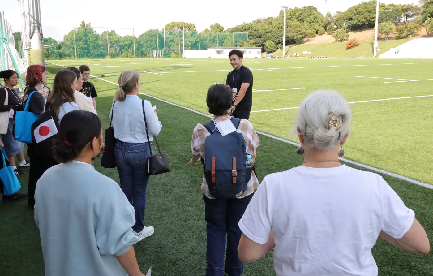 全面人工芝のラグビー場を見学する参加者。さすがラグビー大国で、国際交流センターの中井悠人さんに様々な質問がとんだ 【大阪体育大学】