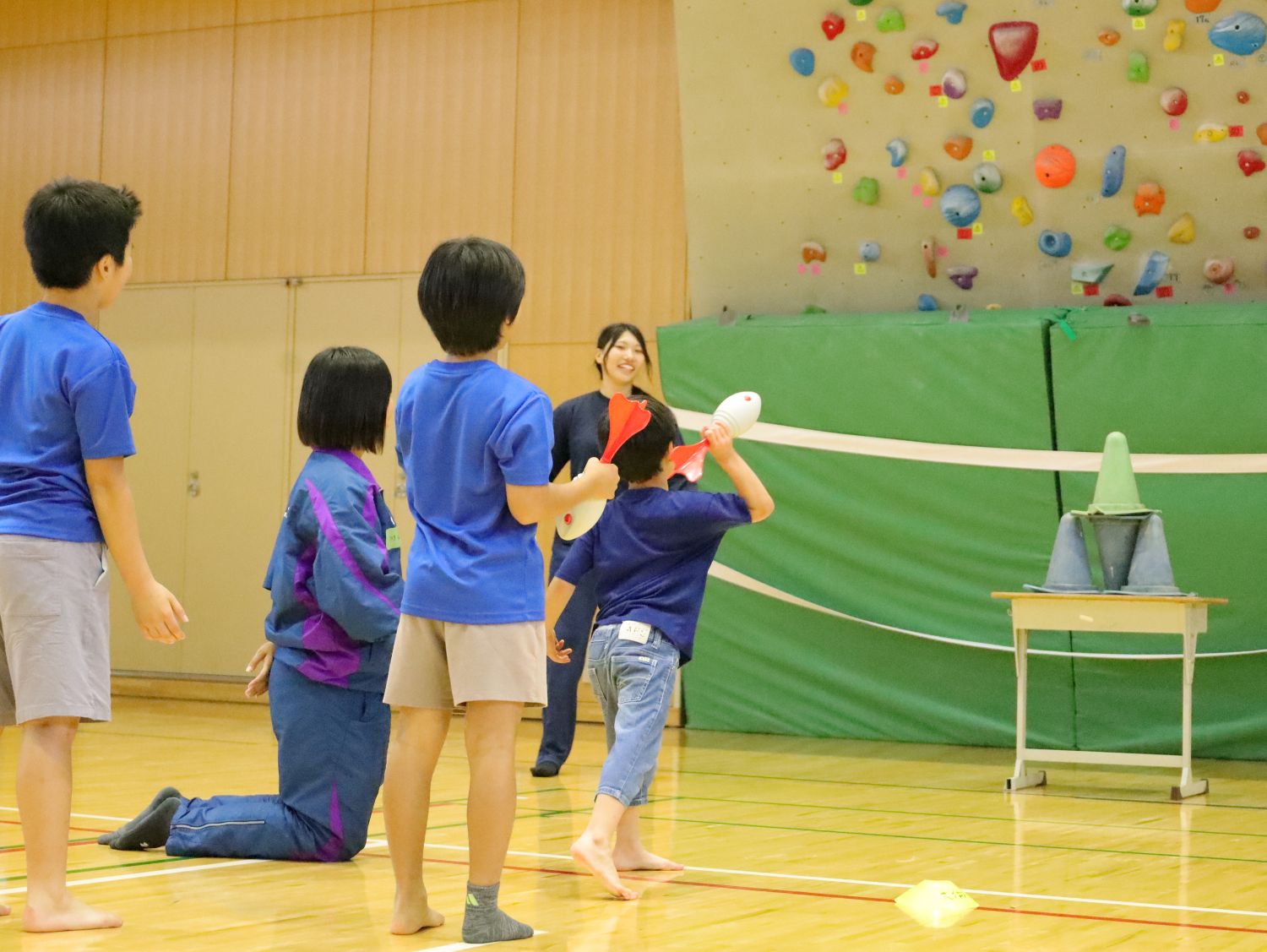 小学生体験会。児童が陸上部員に教えられ、羽根が付いたボールを投げる 【大阪体育大学】
